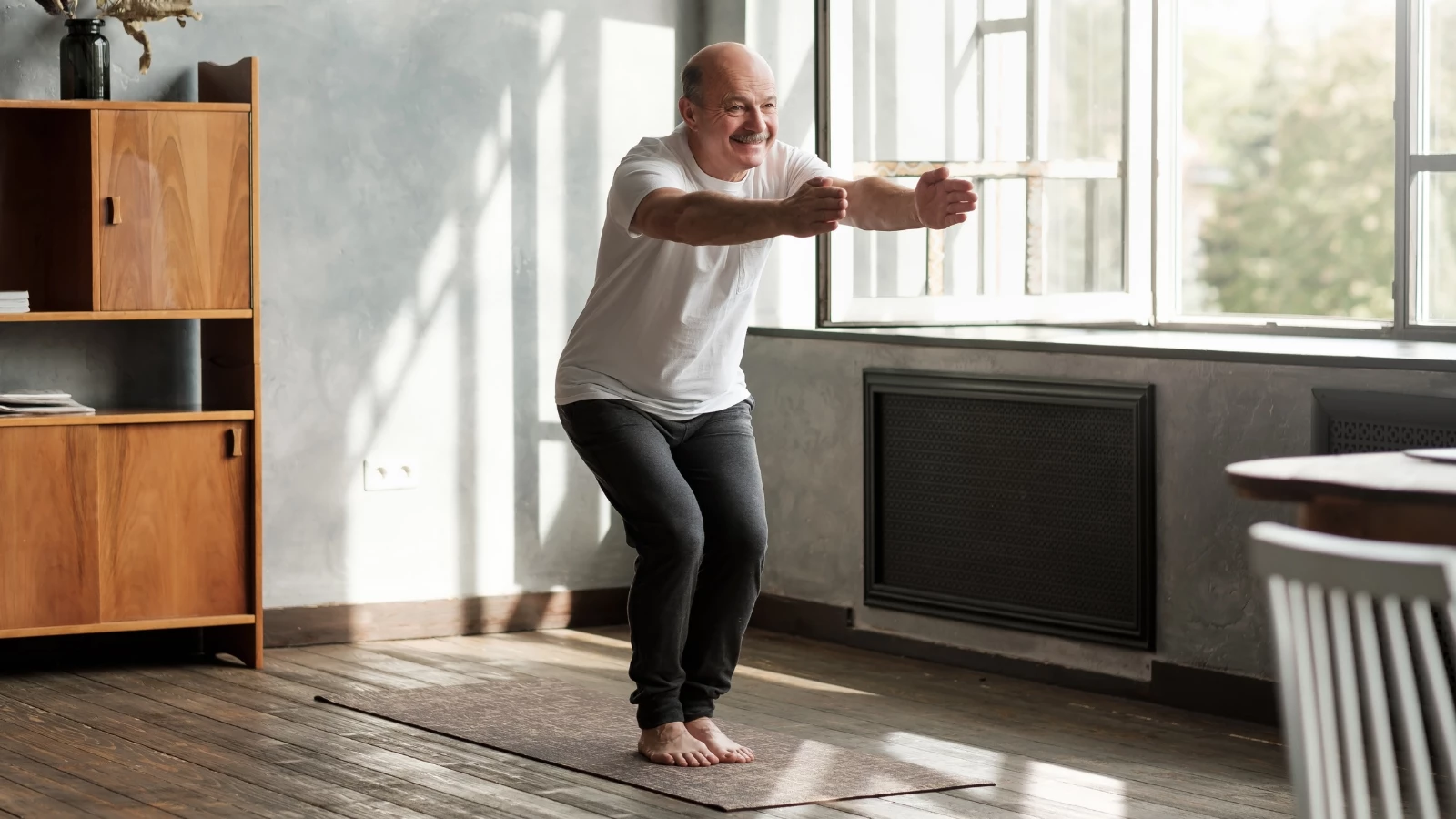 Senior hispanic man practicing Chair pose or Utkatasana indoors in a living room for strong immunity