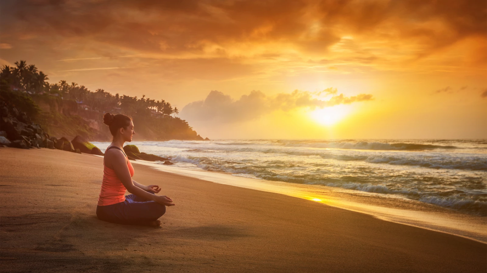 Young woman doing yoga - meditating and relaxing in Padmasana Lotus Pose) with chin mudra outdoors at tropical beach on sunset