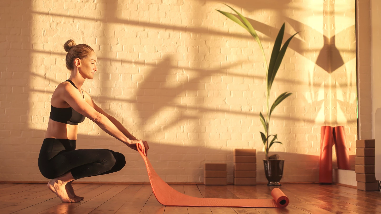 Woman preparing for doing yoga, lying down a mat on the floor in early morning