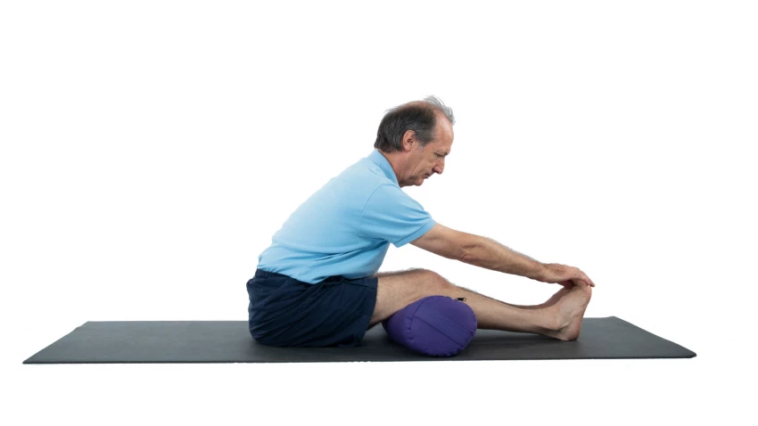 Paschimottanasana Pose or Seated Forward Bend Pose with a bolster under the knees for extra support