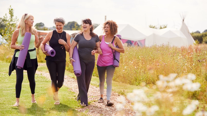 Group Of Mature Female Friends On Outdoor Yoga Retreat Walking Along Path Through Campsite. Yoga and walking are two ways to maximize your exercise benefits.