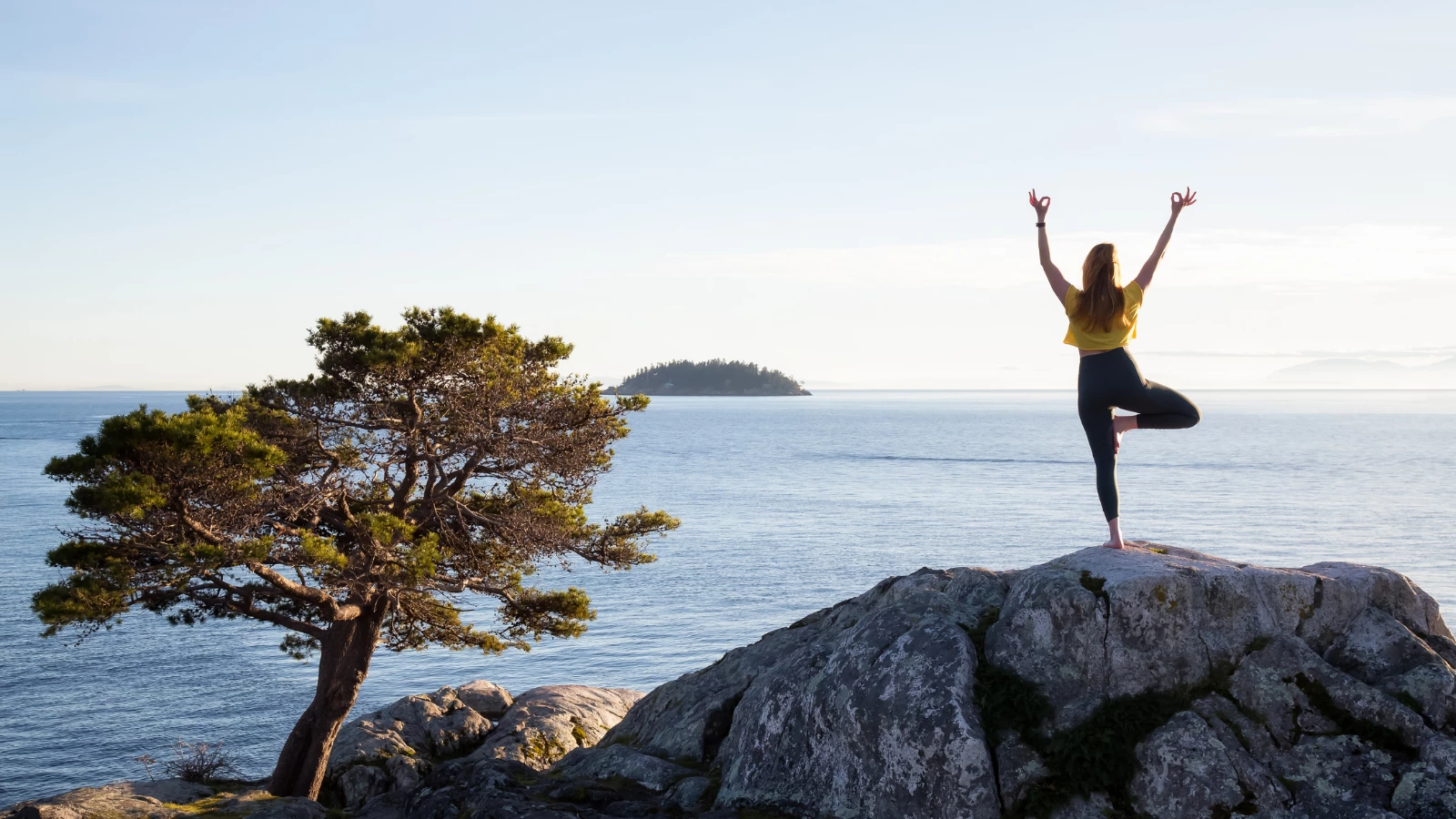 Young woman practicing yoga on a rocky island during a vibrant sunset