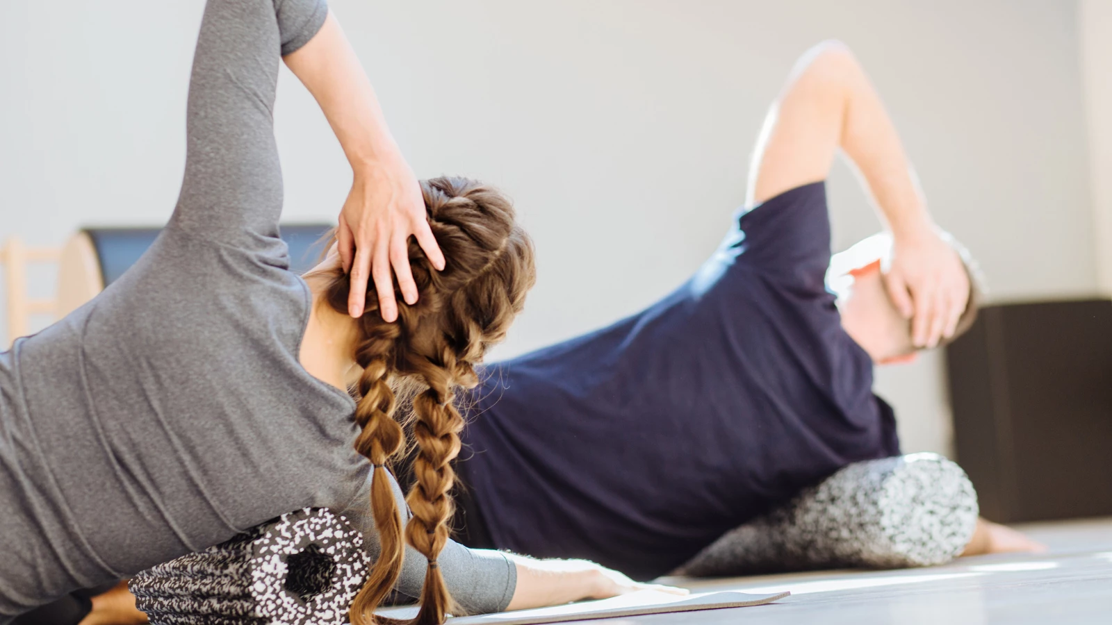 Woman instructor and student performing back exercise with a foam roller