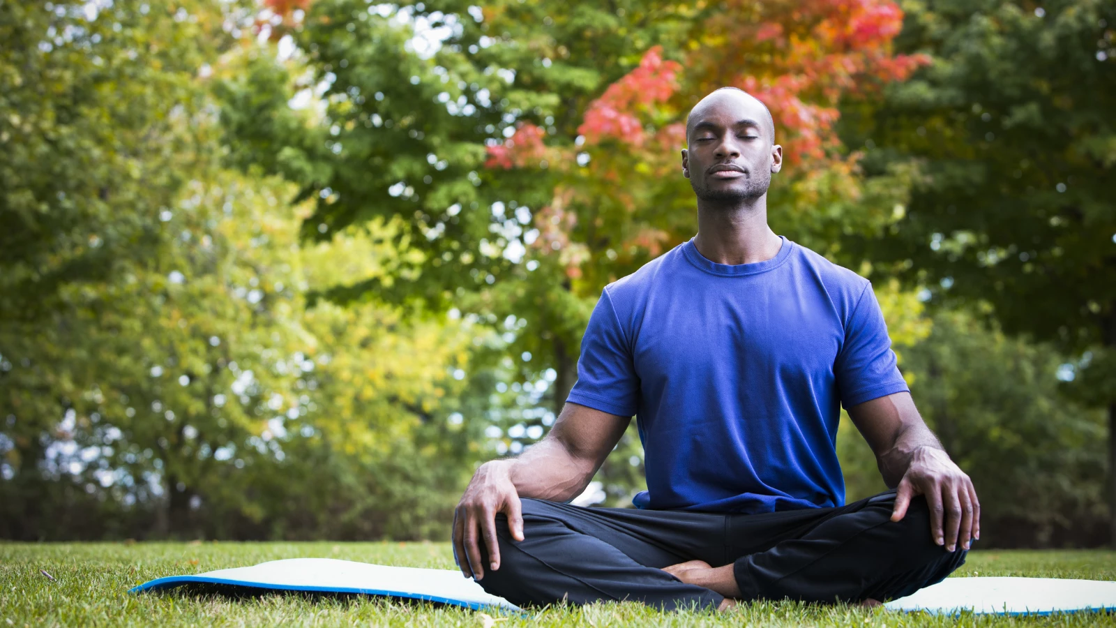 Young man wearing athletic wear sitting in the park practicing Yogic breathing