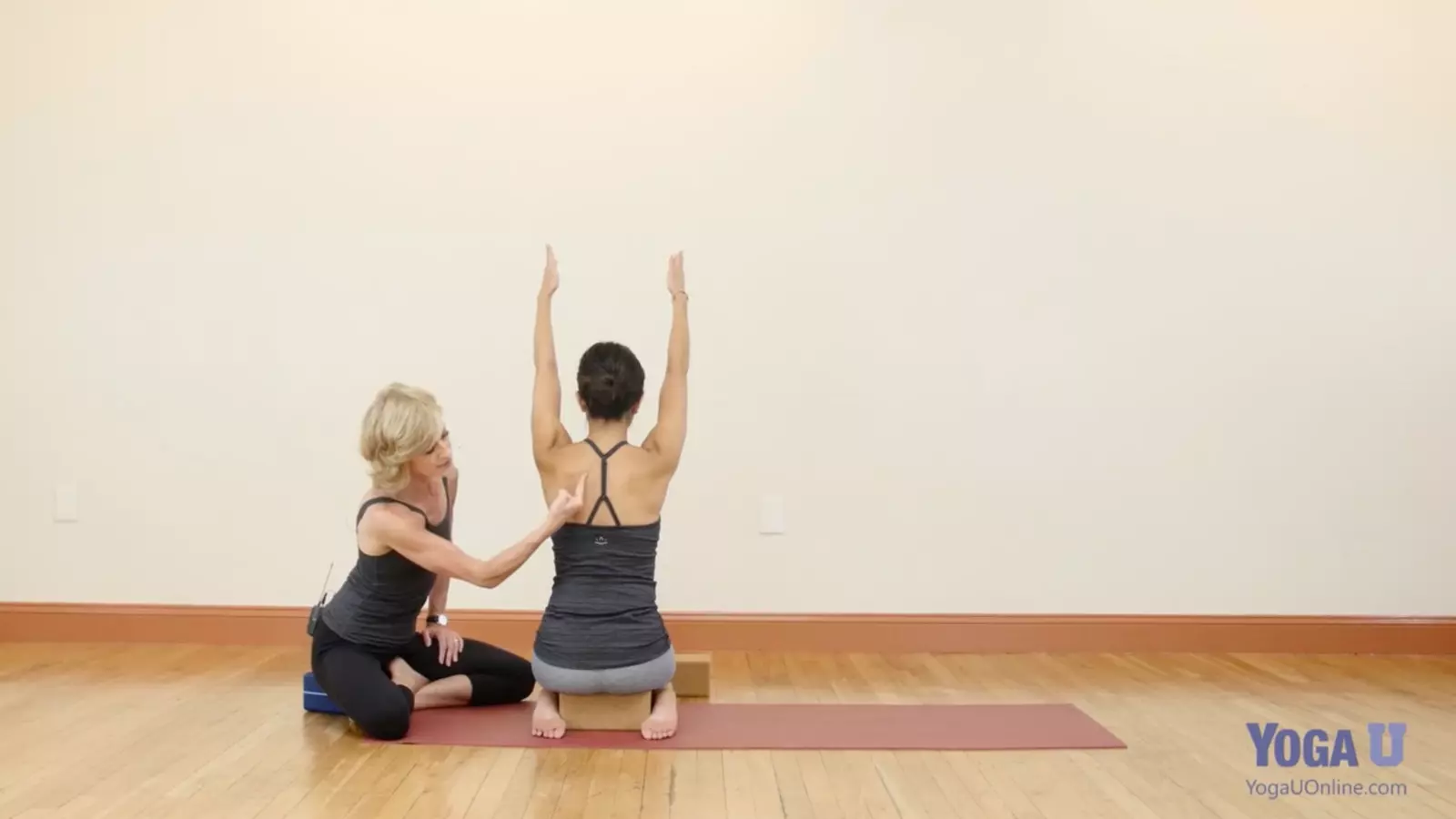 Image depicts teacher and student discussing shoulder alignment for Down Dog Pose. 