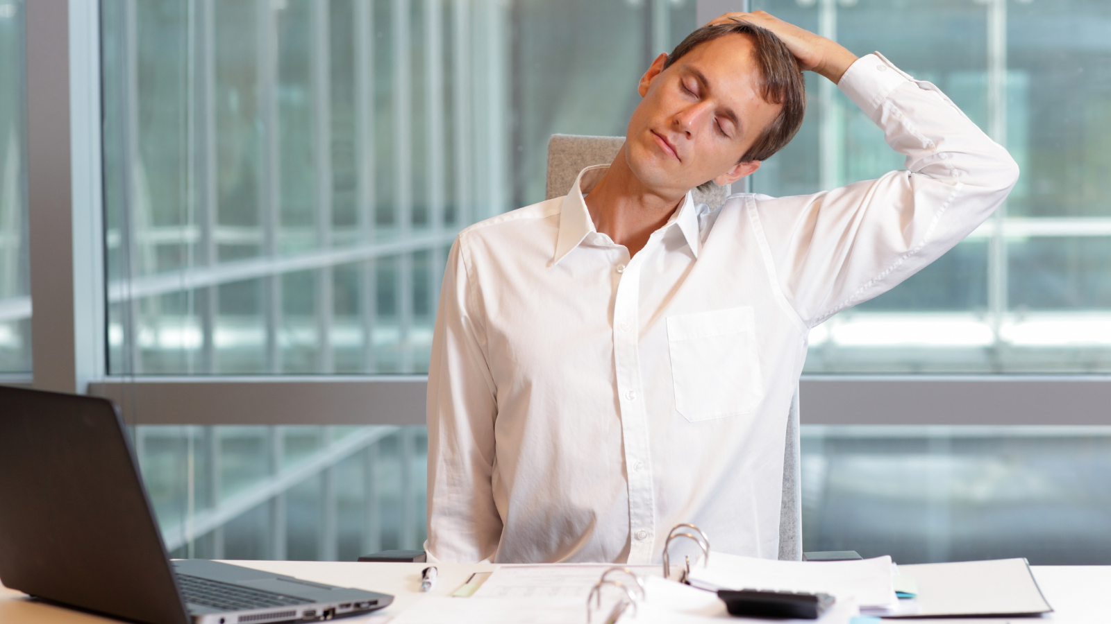 Man working at desk taking the time to do a neck stretch to help keep his neck and shoulders happy and healthy. 