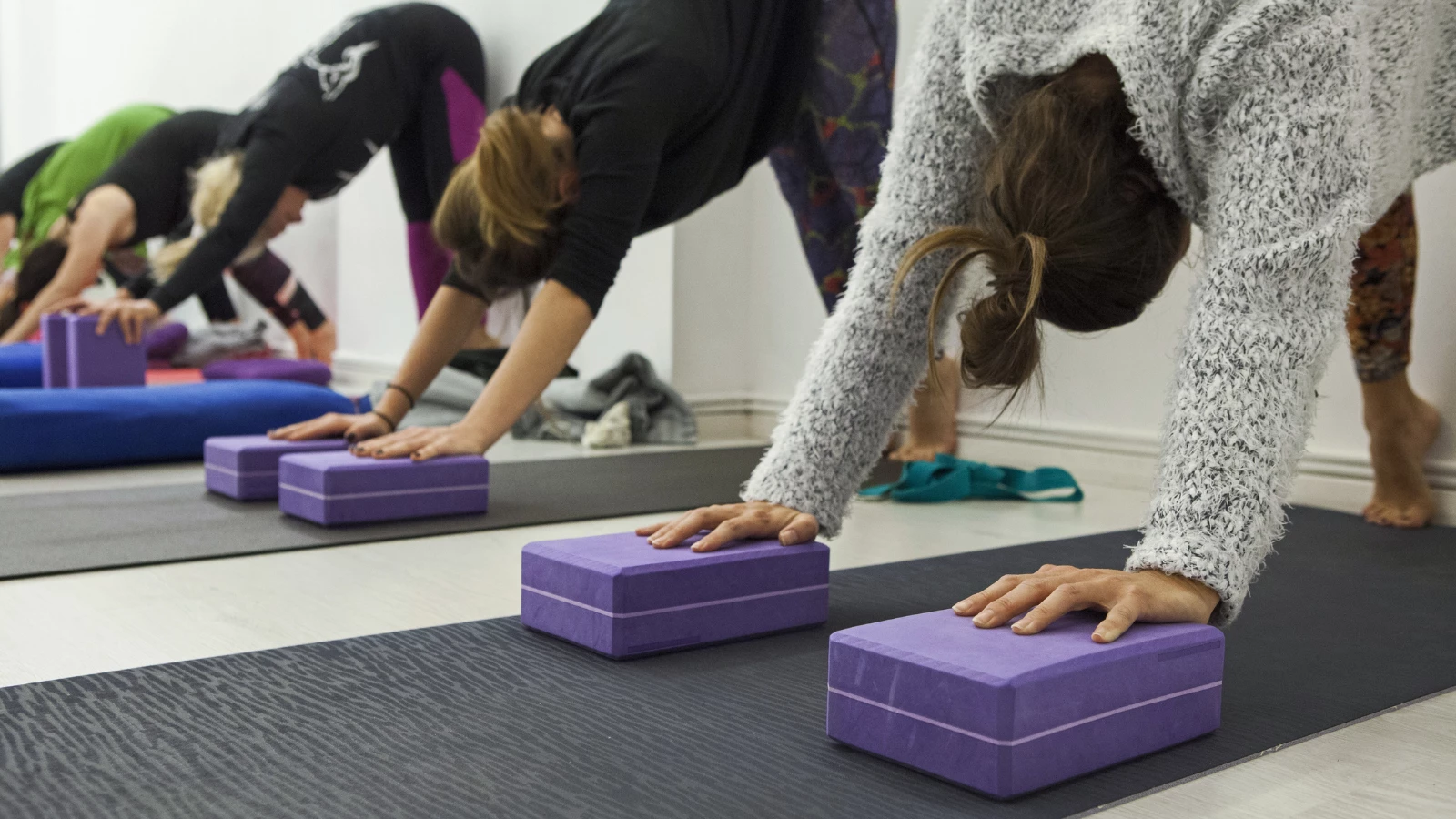 Women stretching in Down Dog using blocks and the wall for comfort and flexibility in the pose