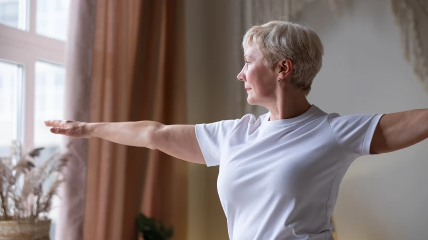 Senior woman performing yoga's Warrior 2 Pose at home.