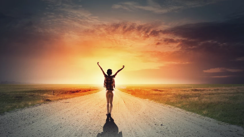 Rear view of girl with hands up facing sunrise.