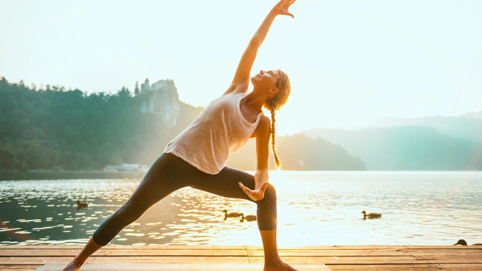 Beautiful woman practicing Yoga by the lake - Sun salutation series - Extended Side Angle Pose.