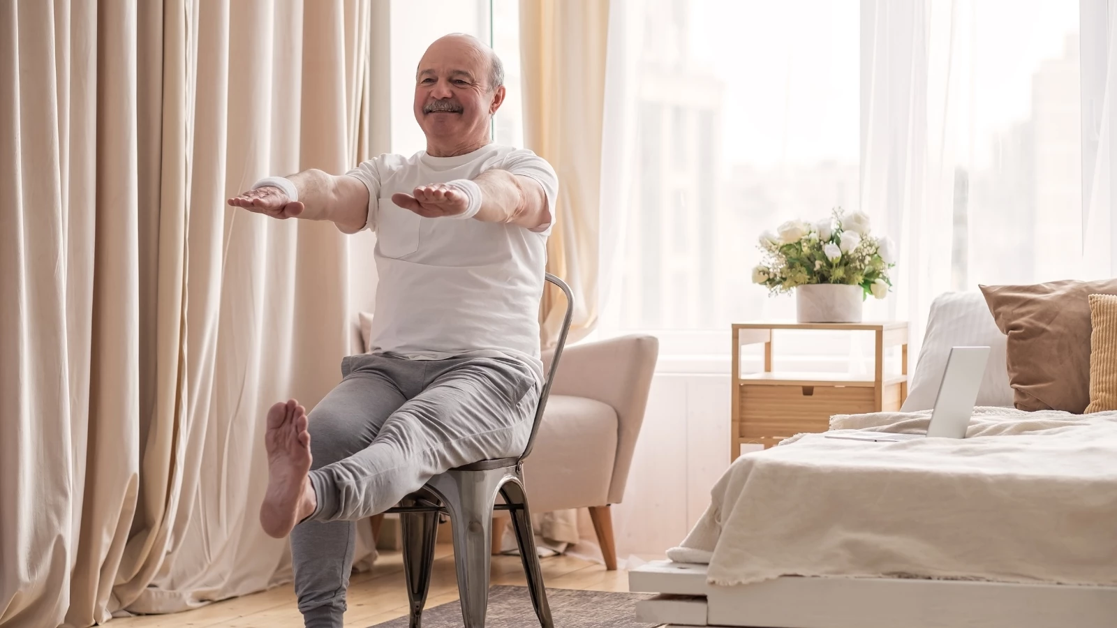 Elderly man practicing yoga asana for legs and arms and hands using chair.