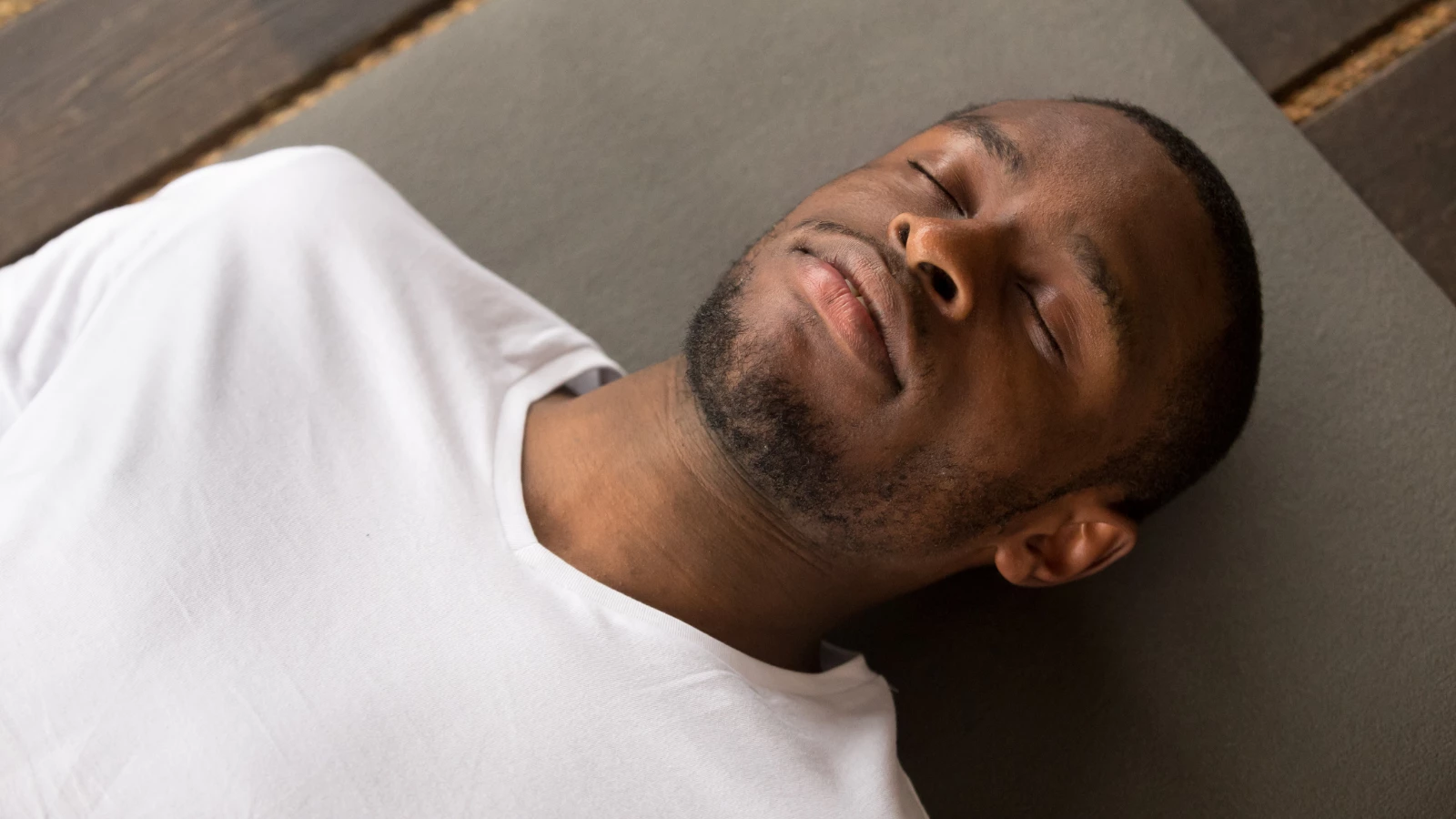 man lying in Savasana or Corpse Pose with his eyes closed resting after practice