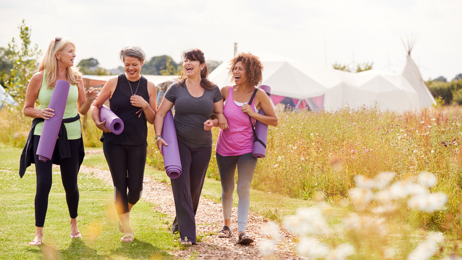 Group Of Mature Female Friends On Outdoor Yoga Retreat Walking Along Path Through Campsite