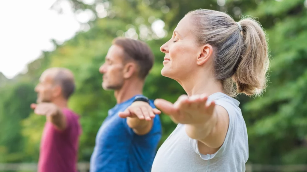 Group of senior people with closed eyes stretching arms at park practing Yoga for Dowager's Hump 