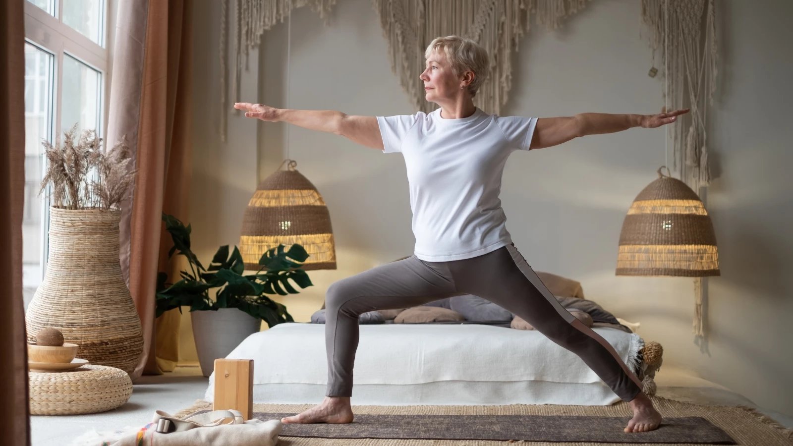 Senior woman practicing yoga, standing in Warrior ll Pose (Virabhadrasana II) working out at home