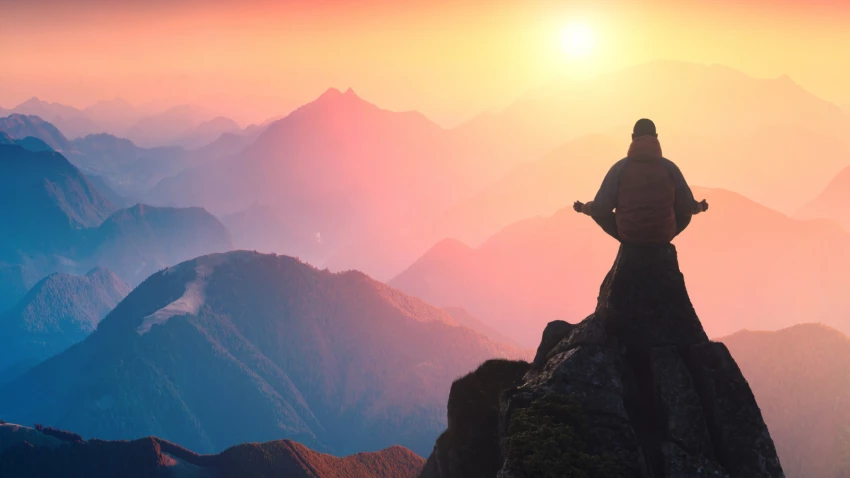 A silhouette of a person meditating on top of a mountain above a misty valley.