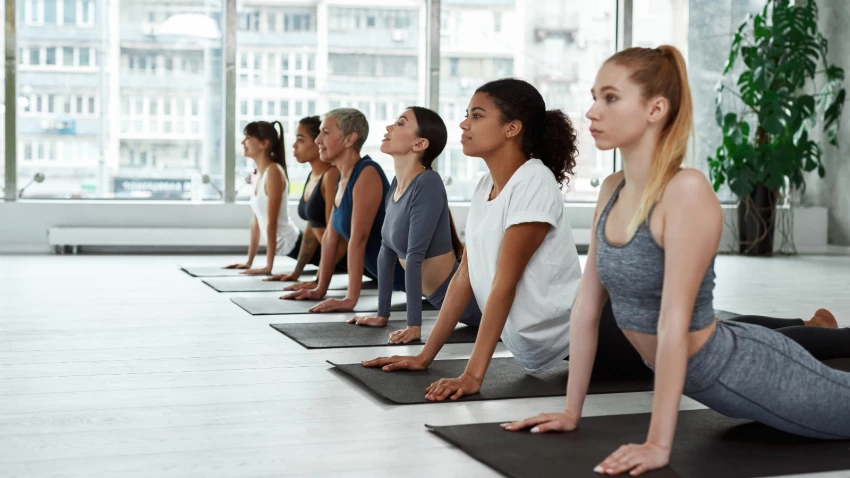 Image depicts a diverse group of yoga students at class practicing Bhujangasana or Cobra Pose.