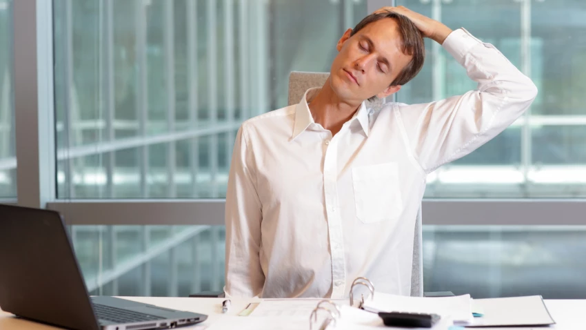 Young man at his work desk taking a break to do some neck stretches