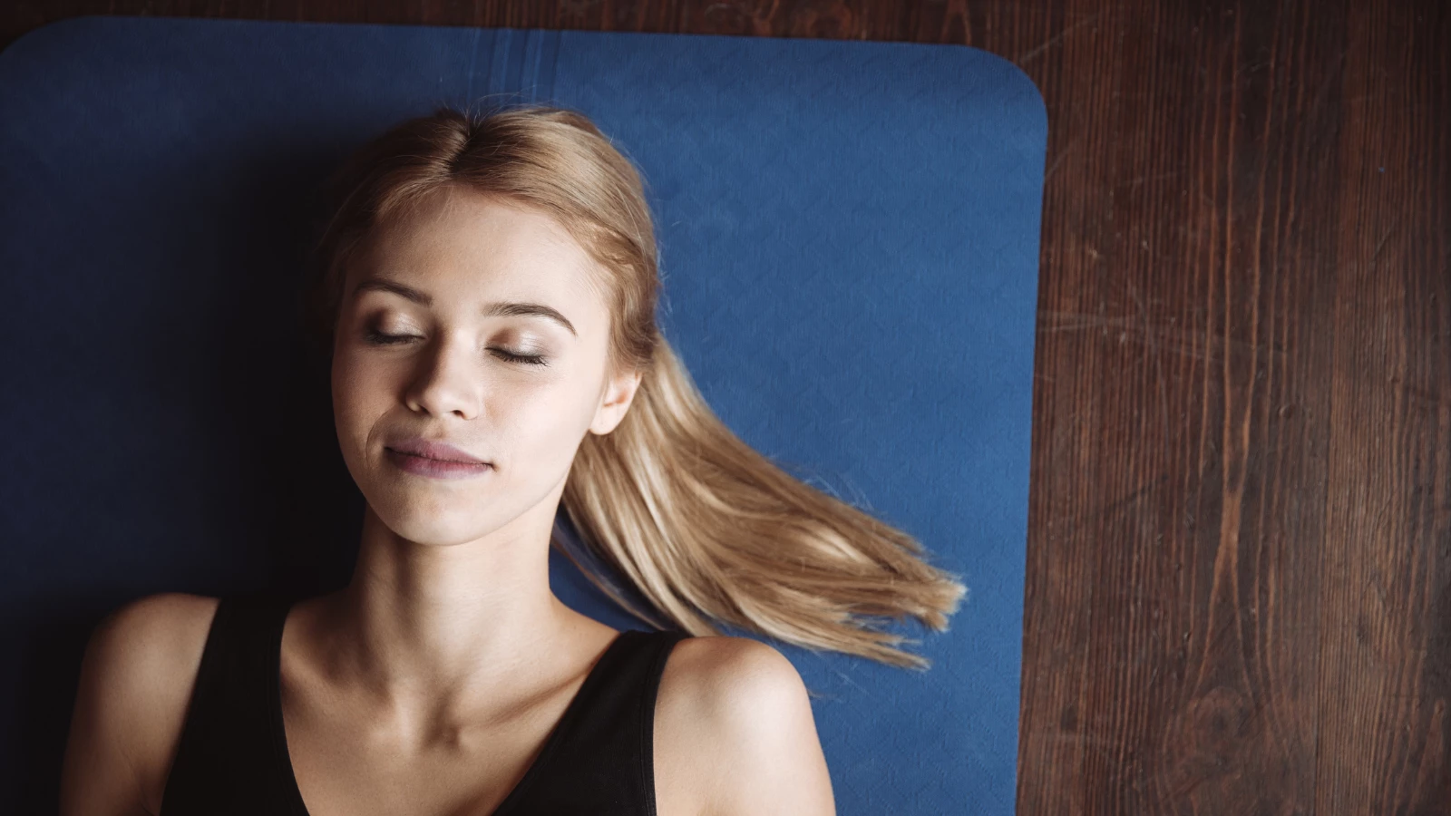 Top view of cute young fitness woman lying on the floor on mat with eyes closed.