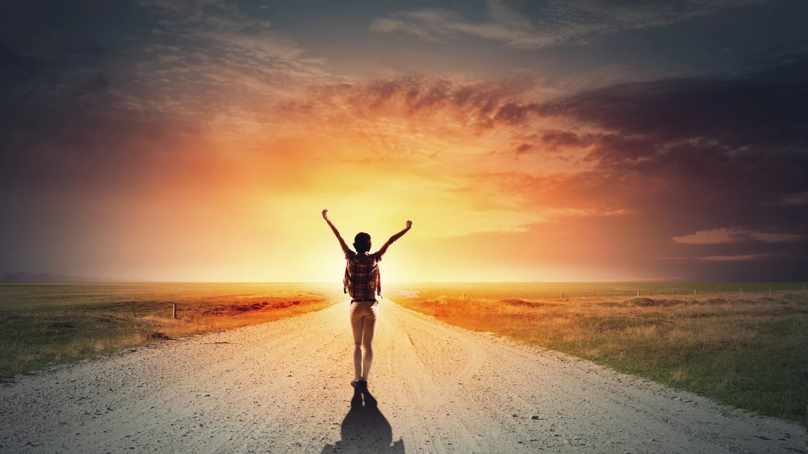 woman raising her arms in joy walking on road towards a sunset, depicting feeling of self-healing