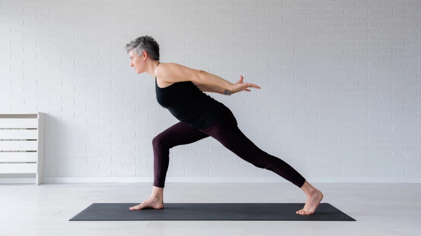 Mature woman practicing a Warrior 1 variation.