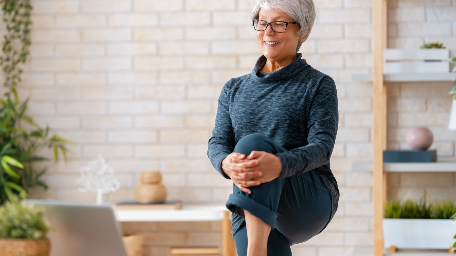 Senior woman in activewear watching online courses on laptop while exercising at home.