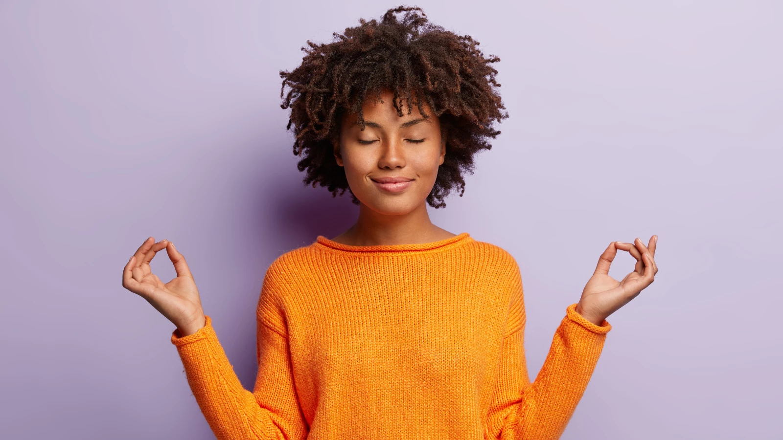 woman in orange clothes meditates indoor, holds hands in mudra gesture