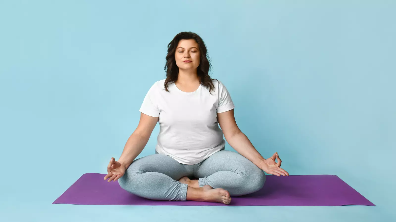 Beautiful plus size woman meditating against pretty blue color background.