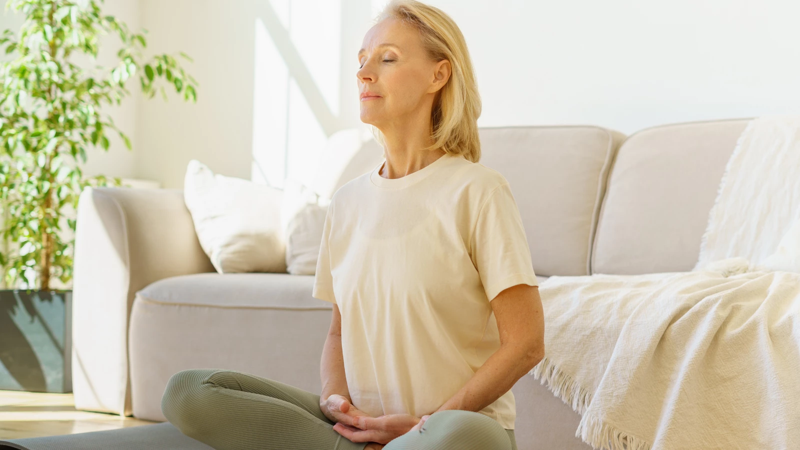 senior woman in lotus position meditation with closed eyes at home while sitting on yoga mat