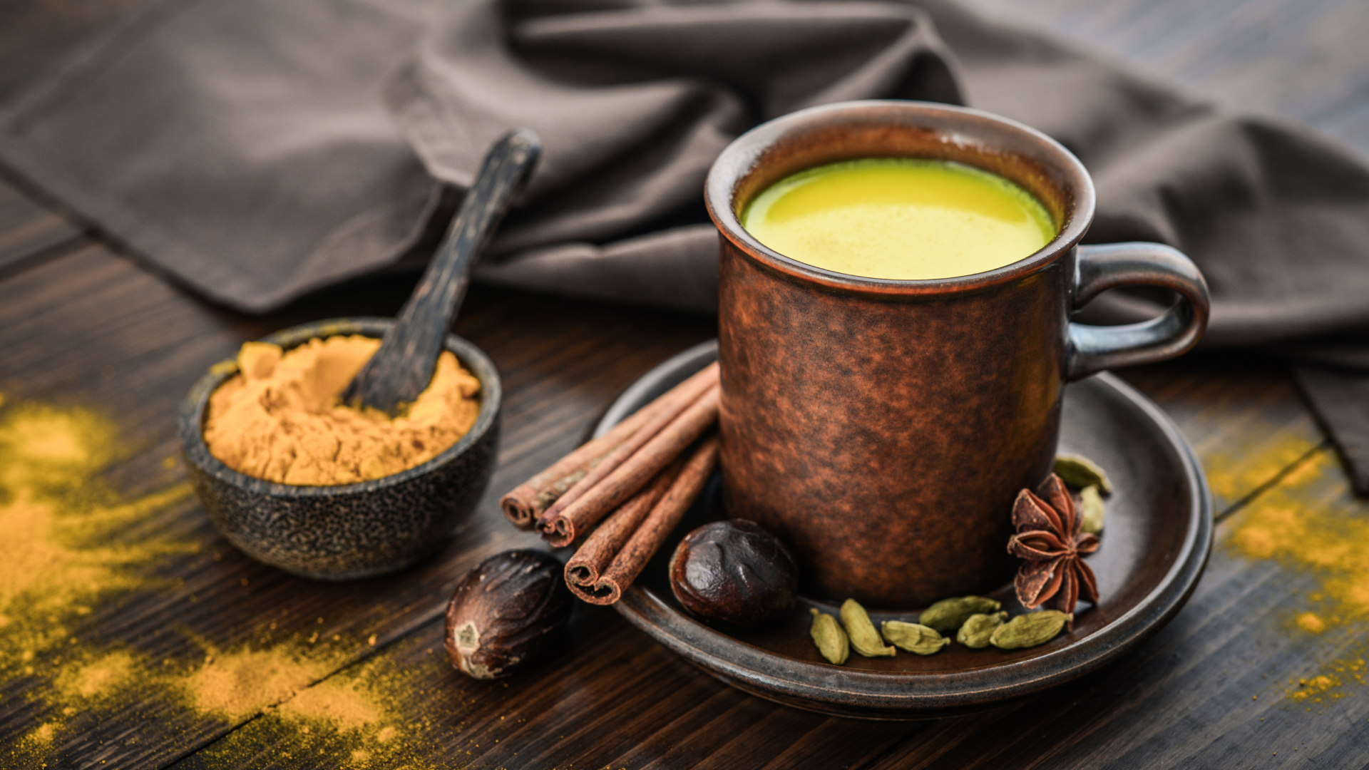 Traditional Indian drink turmeric milk is golden milk with cinnamon, cloves, pepper and turmeric on a wooden background with spices to induce sleep for a healthy wake up early routine. 