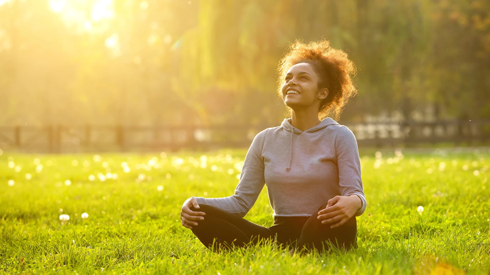 Happy young woman sitting outdoors in yoga's Easy Pose resting and enjoying nature.