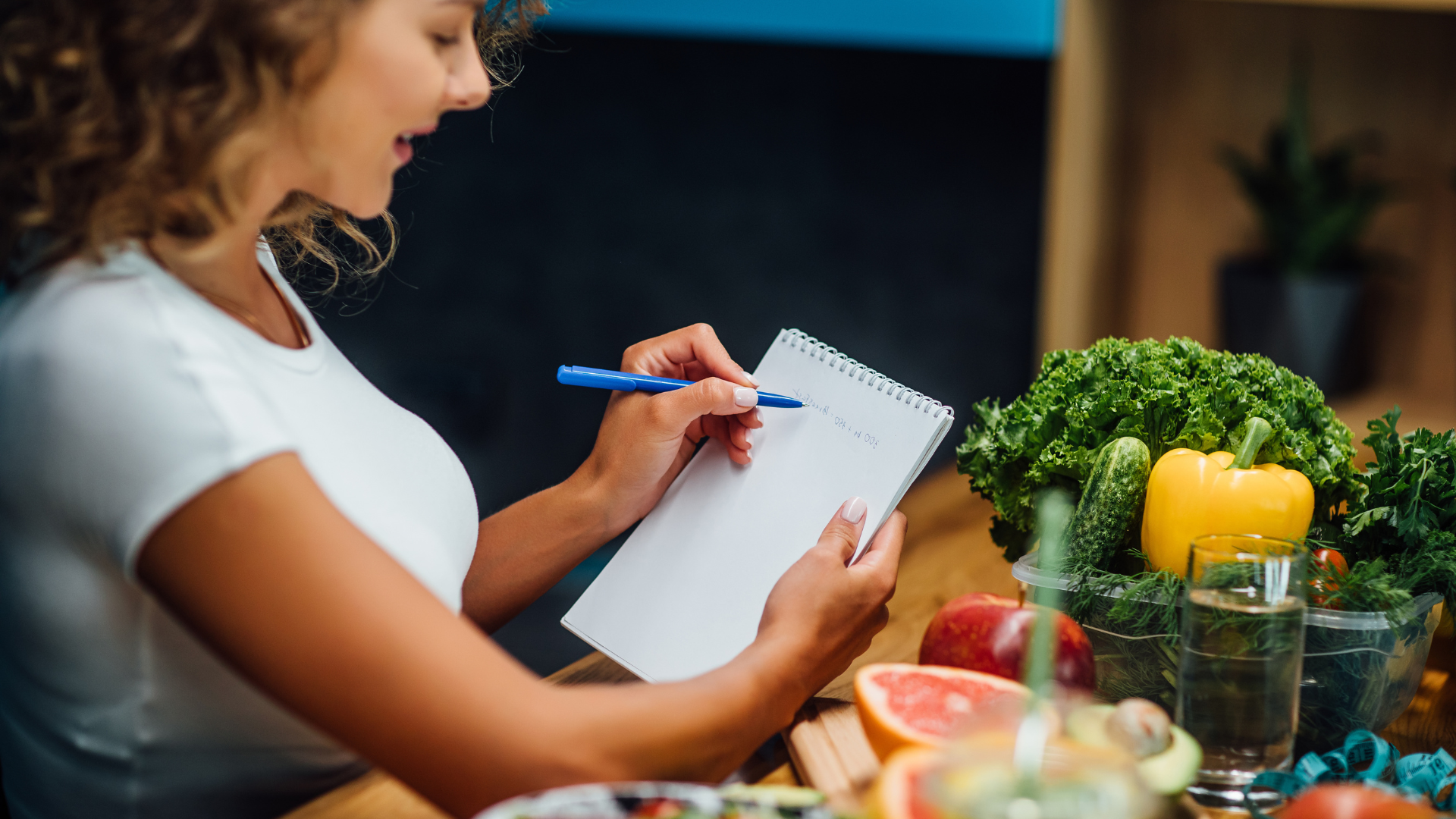  Nutritionist working in office writing diet plan surrounded by fruits and vegetables. 