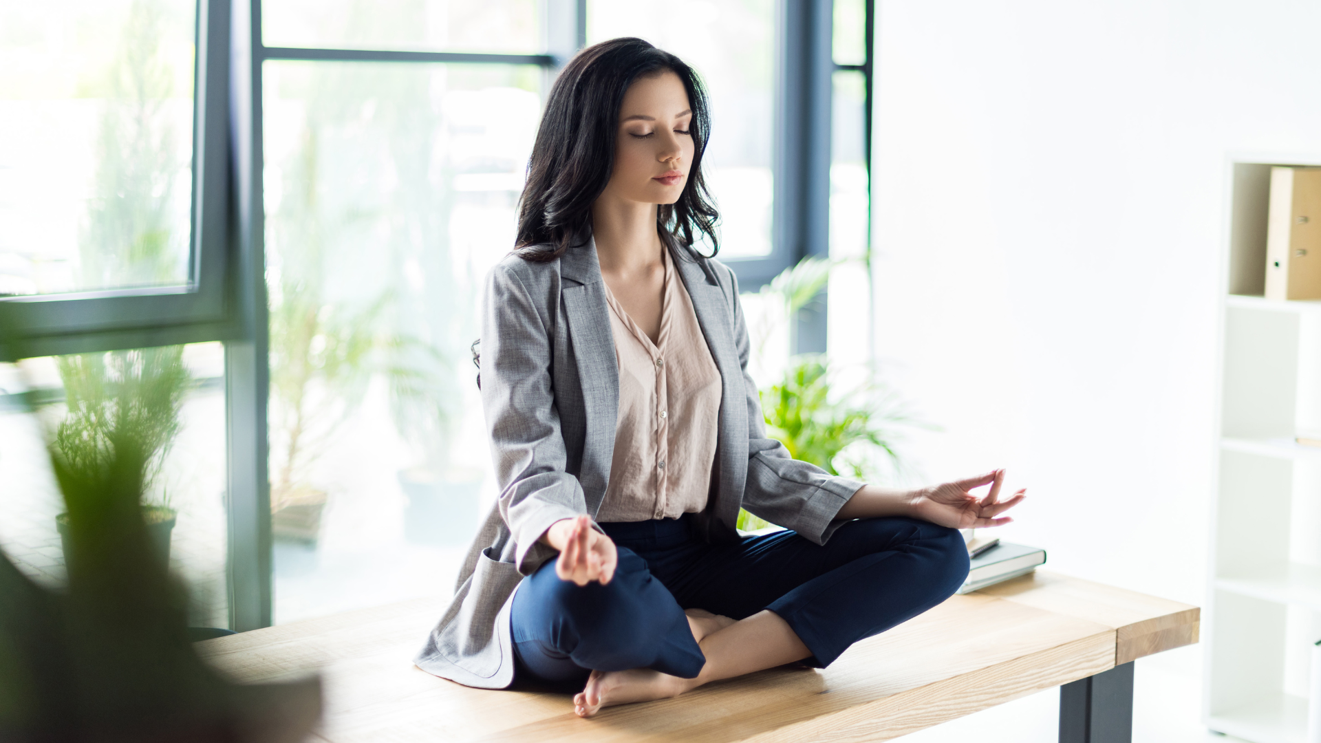 Relaxed businesswoman with eyes closed meditating, a spiritual practice, at office workplace.