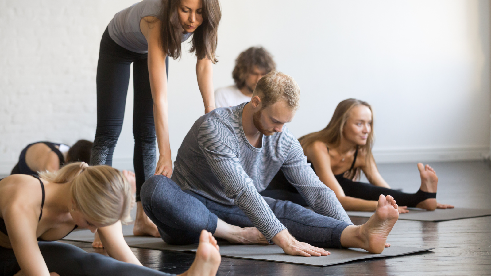 Young yoga instructor teaching Head to Knee Forward Bend pose, Janu Sirsasana Pose offering individual attention as a great way to create a yoga teaching niche.