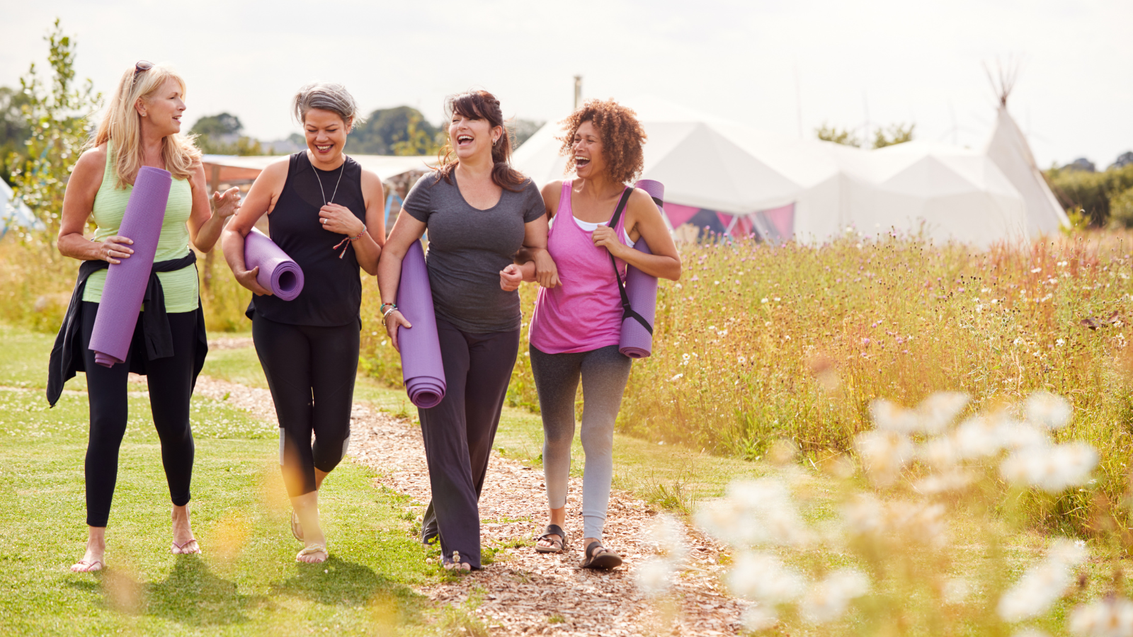 Group Of Mature Female Friends On Outdoor Yoga Retreat Walking Along Path Through Campsite