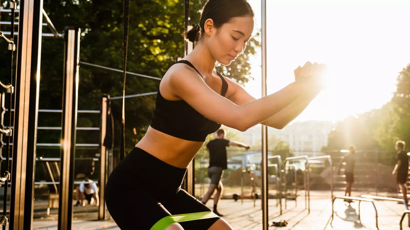 Asian woman doing exercise with resistance band during workout on playground outdoors.