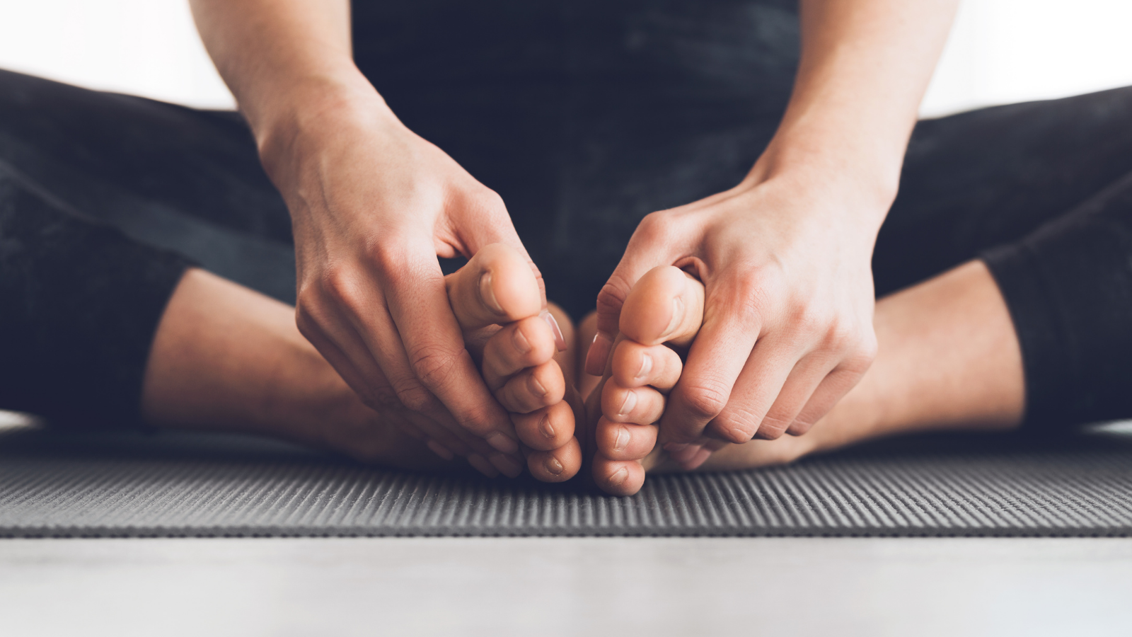 Woman sitting in lotus position with bare feet, practicing yoga at home.