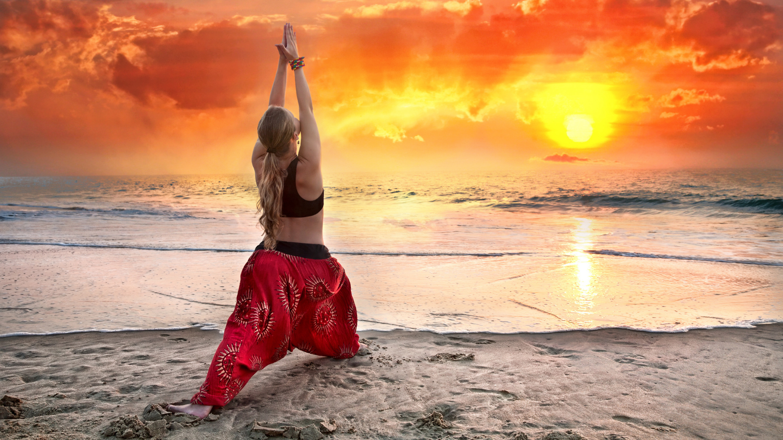 Beautiful woman doing virabhadrasana I, warrior yoga pose on the beach near the ocean at sunset in India