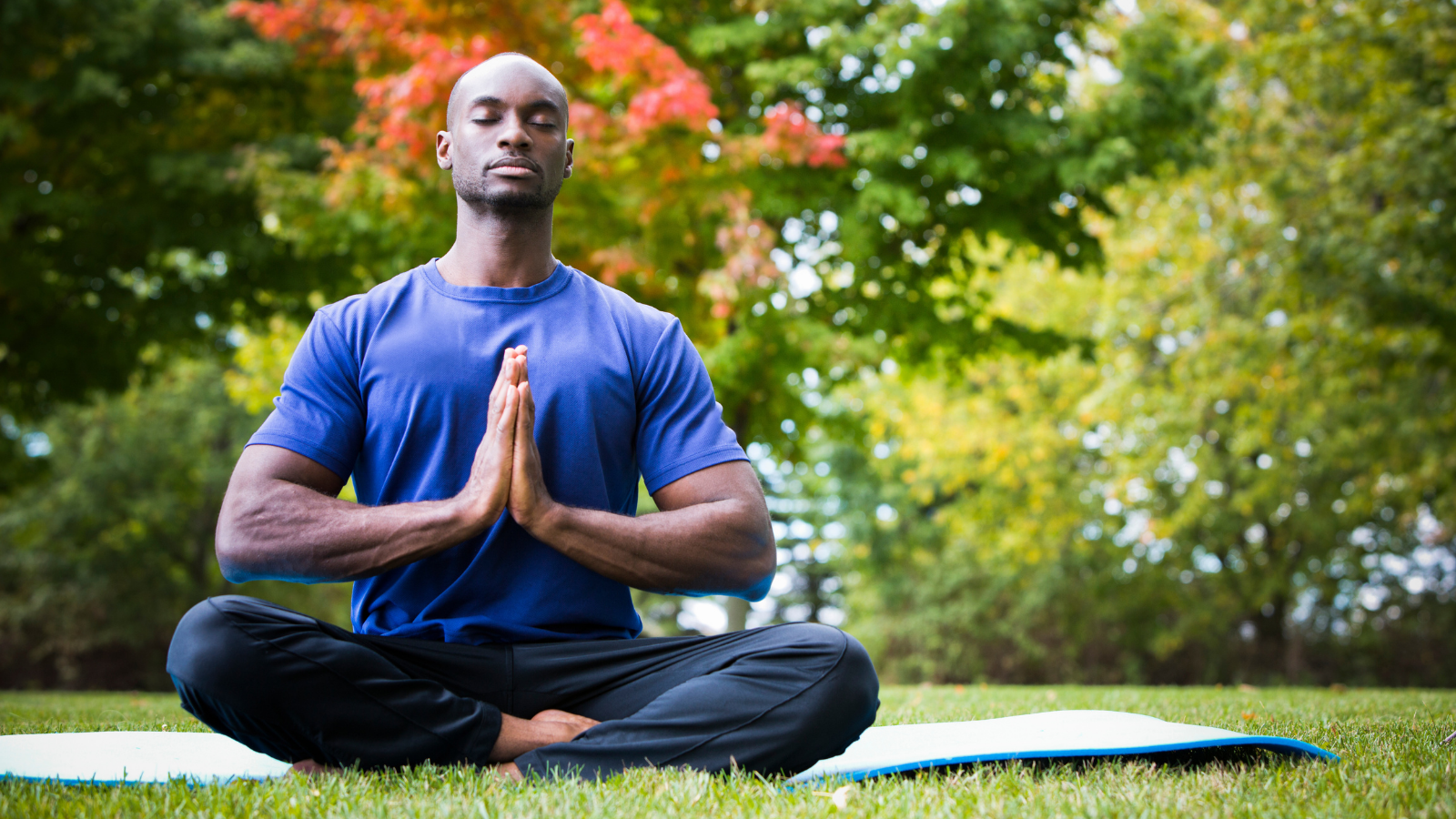 young black man wearing athletic wear sitting in the park practicing yoga