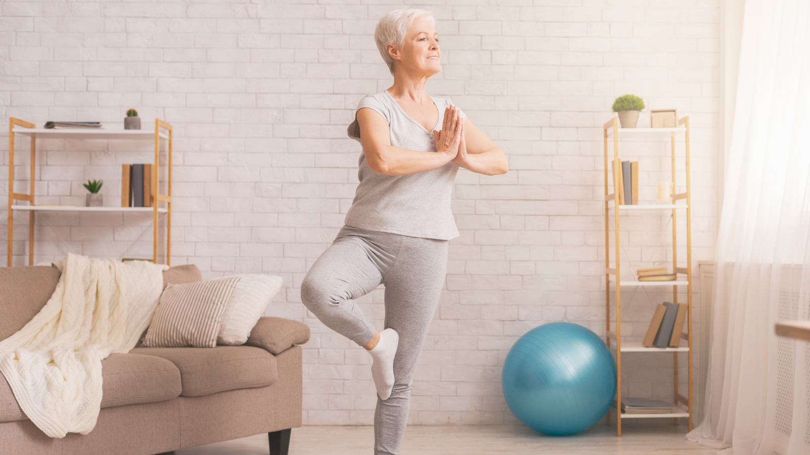 A senior woman doing Tree Pose (Vrikshasana) at home.