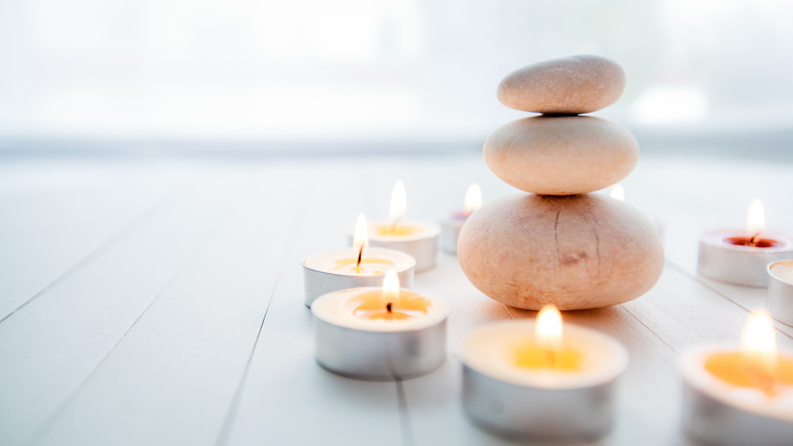 A healing yoga scene depicting a balanced stack of stones with aromatic candles on wooden white background.