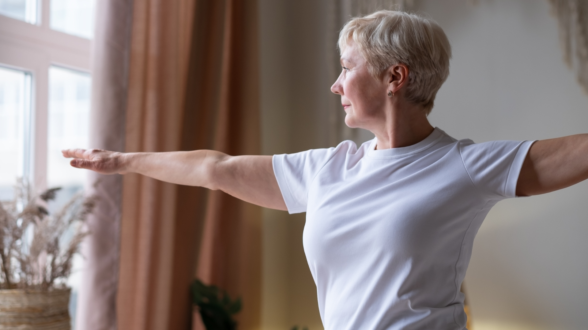 A senior woman practicing Virabhadrasana II (Warrior II Pose) at home