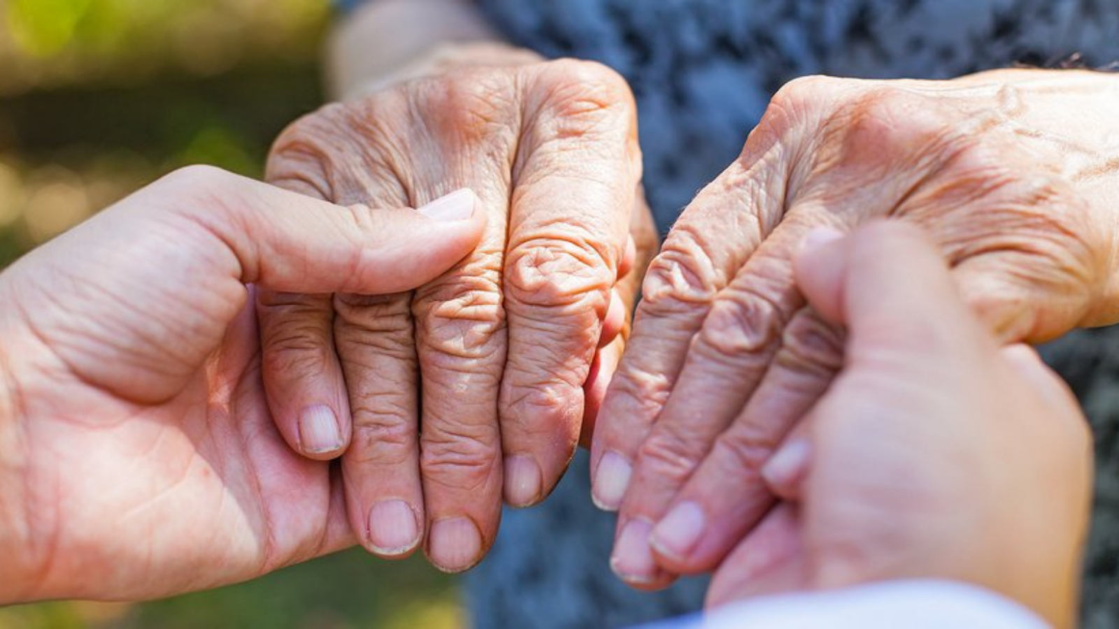 Senior with Parkinson's disease holding hands holding hands with a family member.