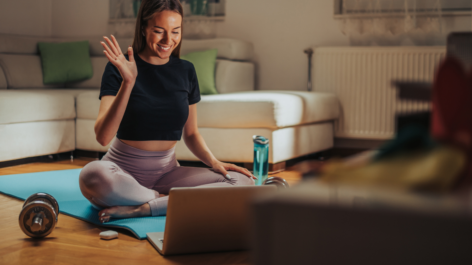 Young attractive woman using laptop while having an online fitness training with a professional instructor while at home