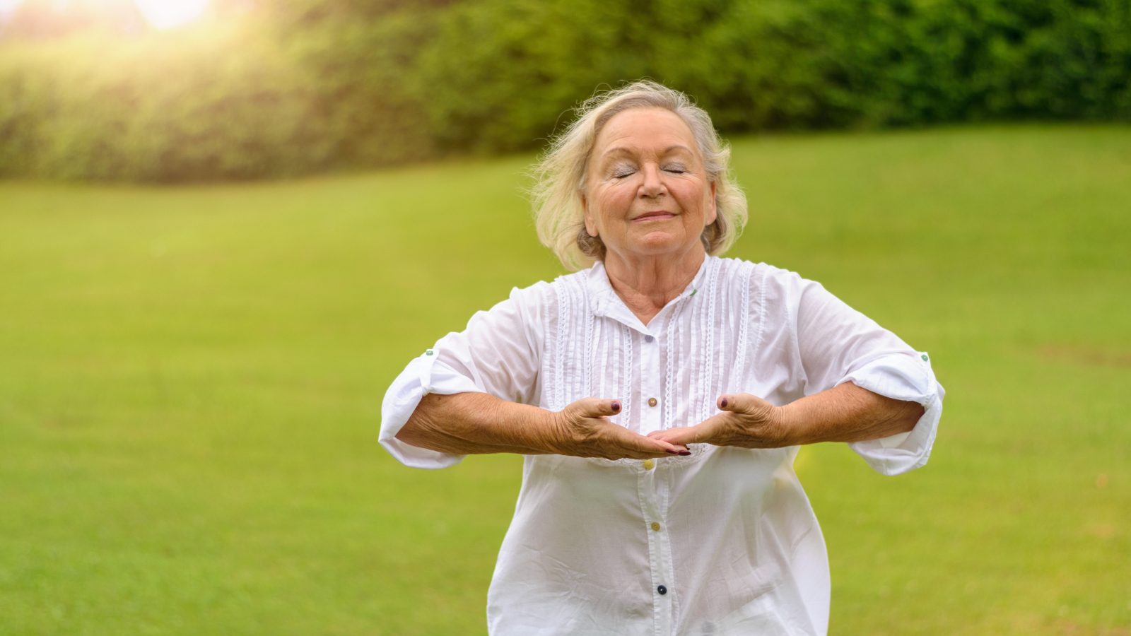 Beautiful senior woman in white rolled up long sleeve blouse practicing breathing exercises outside with eyes closed.