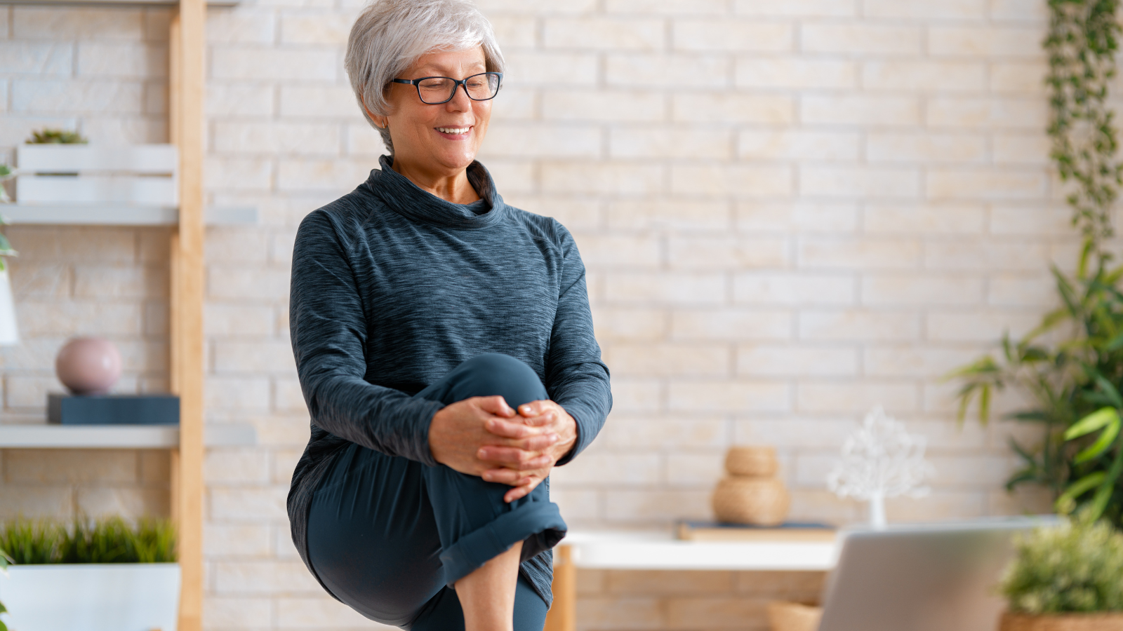 Senior woman in activewear watching online courses on laptop while exercising at home.