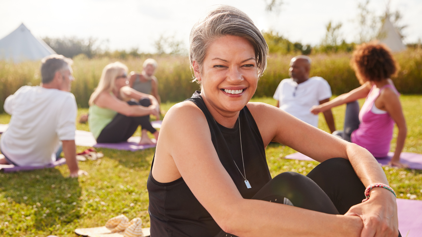 Portrait Of Mature Woman On Outdoor Yoga Retreat With Friends And Campsite In Background.