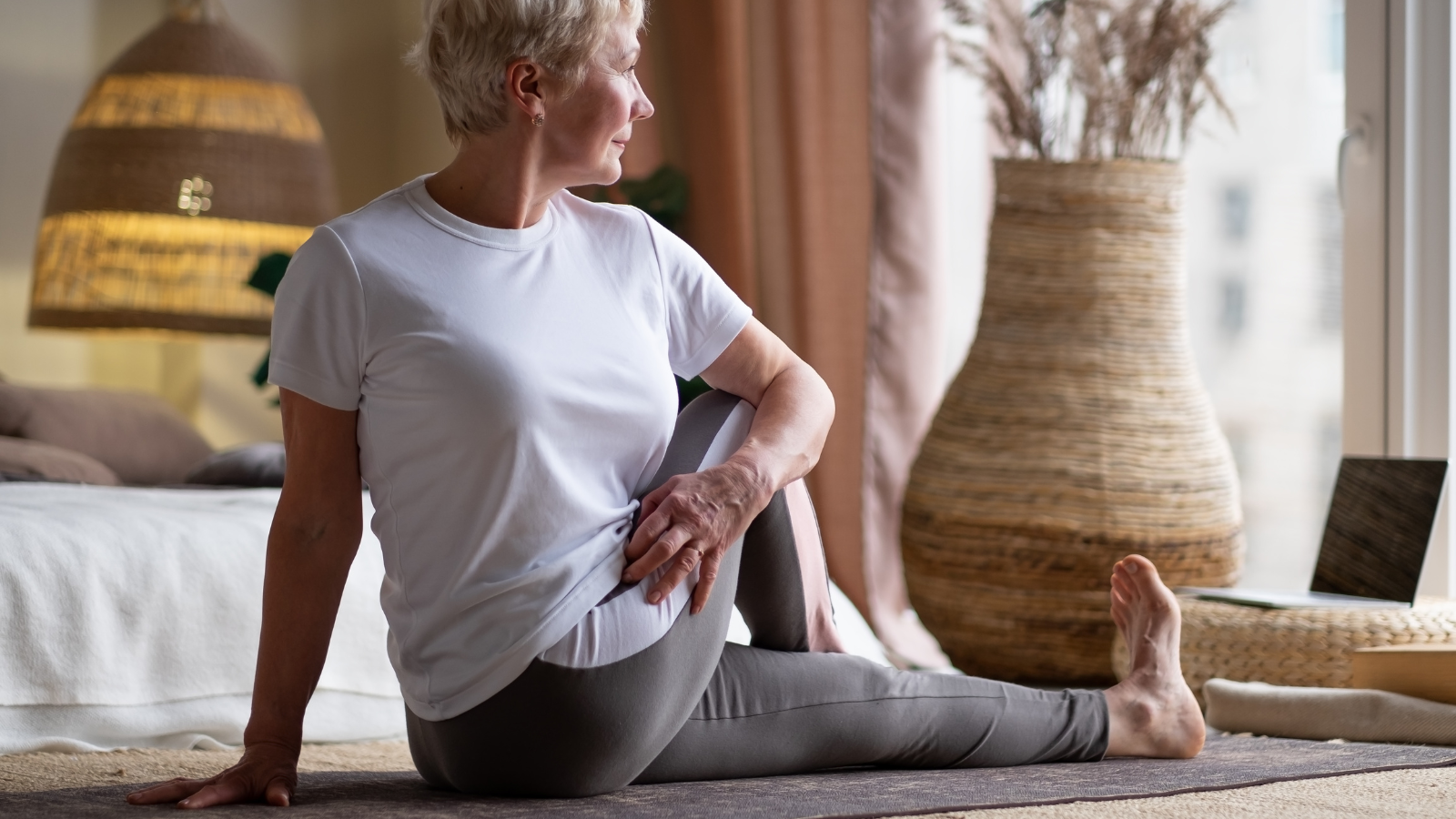 Senior woman in half spinal twist pose on mat at home. 