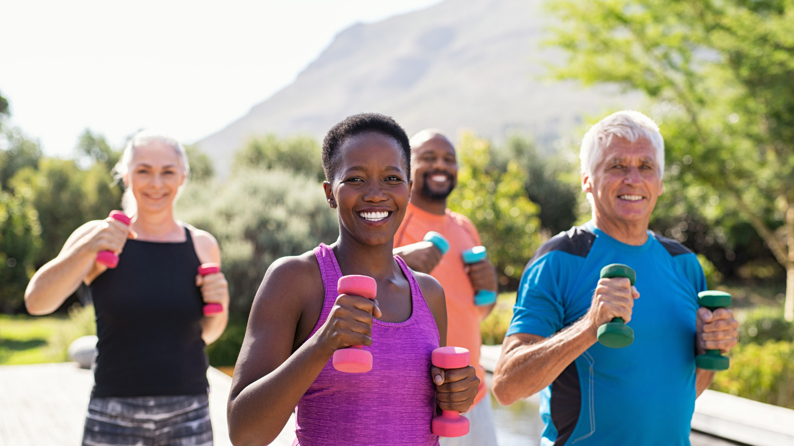 Group of mature happy people using dumbbells for workout session. Diverse group of smiling women and senior men exercising with dumbbells while walking outdoors. 