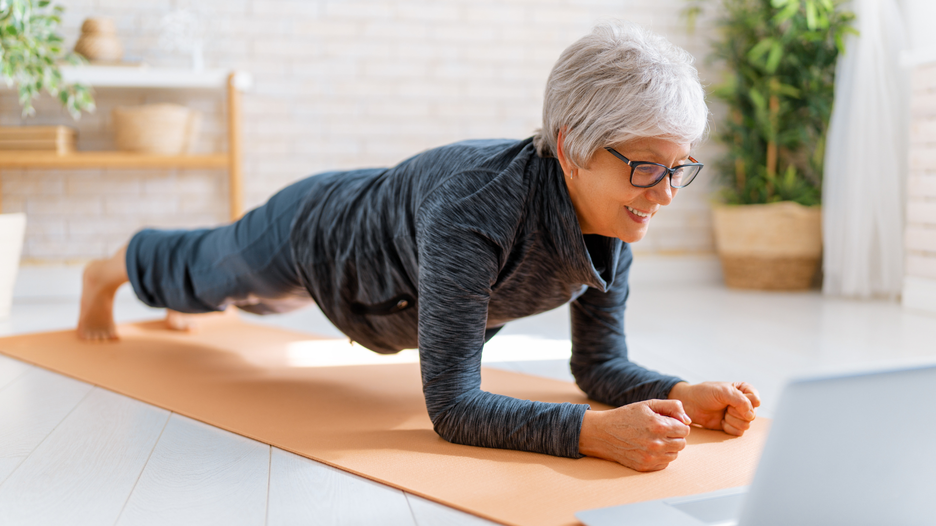 Senior woman in activewear watching online courses on laptop while practicing yoga at home. 